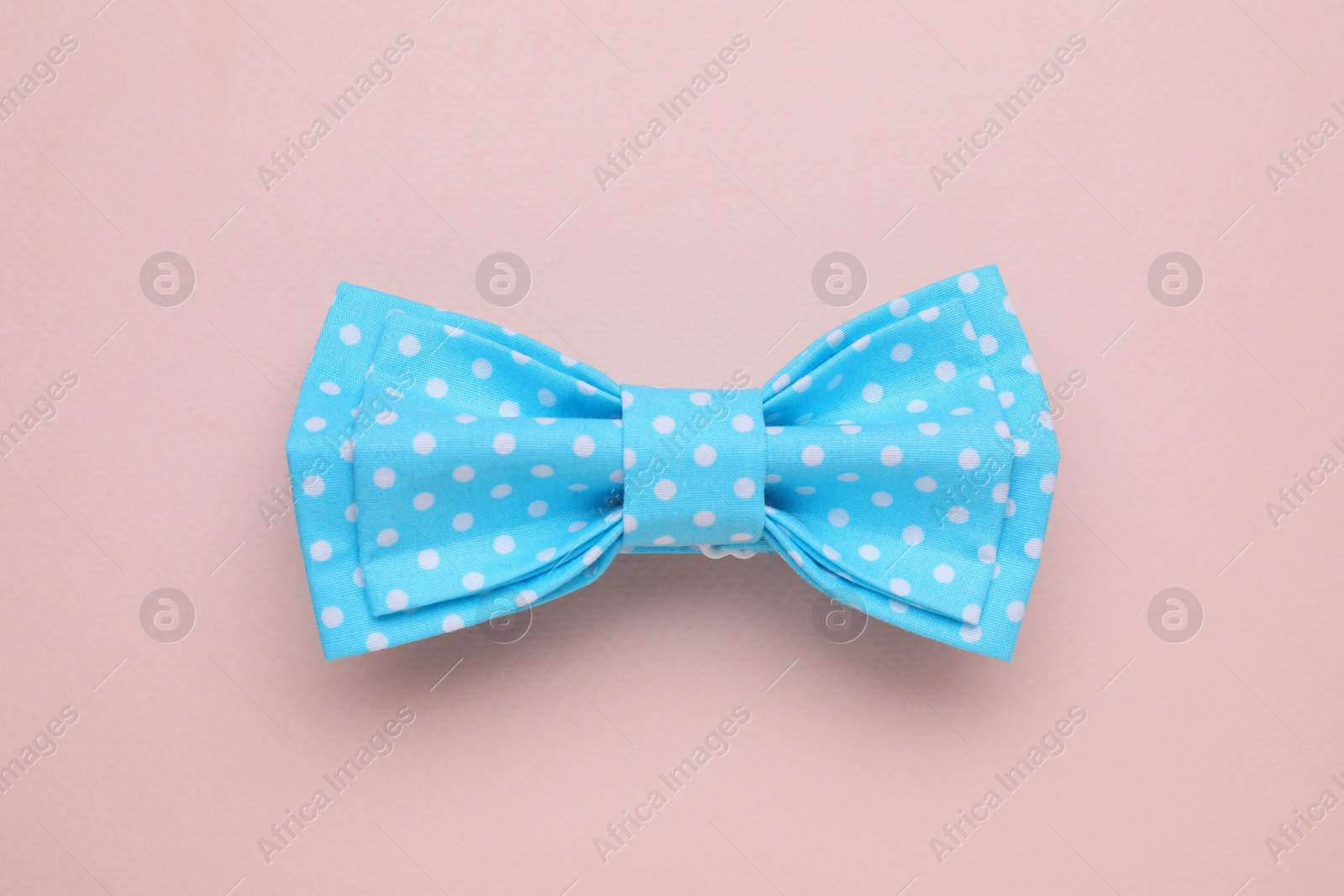 Photo of Stylish light blue bow tie with polka dot pattern on beige background, top view