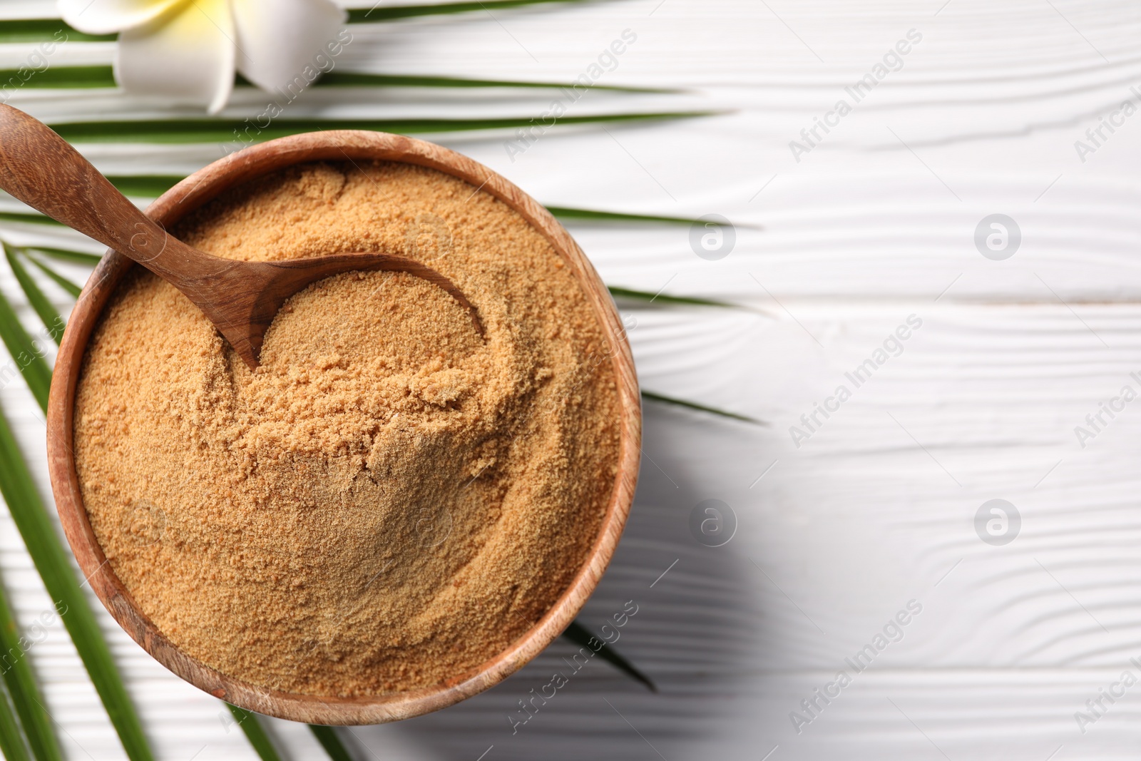 Photo of Coconut sugar and spoon in bowl on white wooden table, flat lay. Space for text