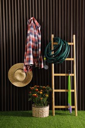 Beautiful blooming marigolds, gardening tools and accessories on green grass near wood slat wall