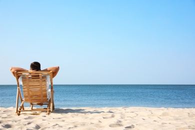 Photo of Young man relaxing in deck chair on sandy beach