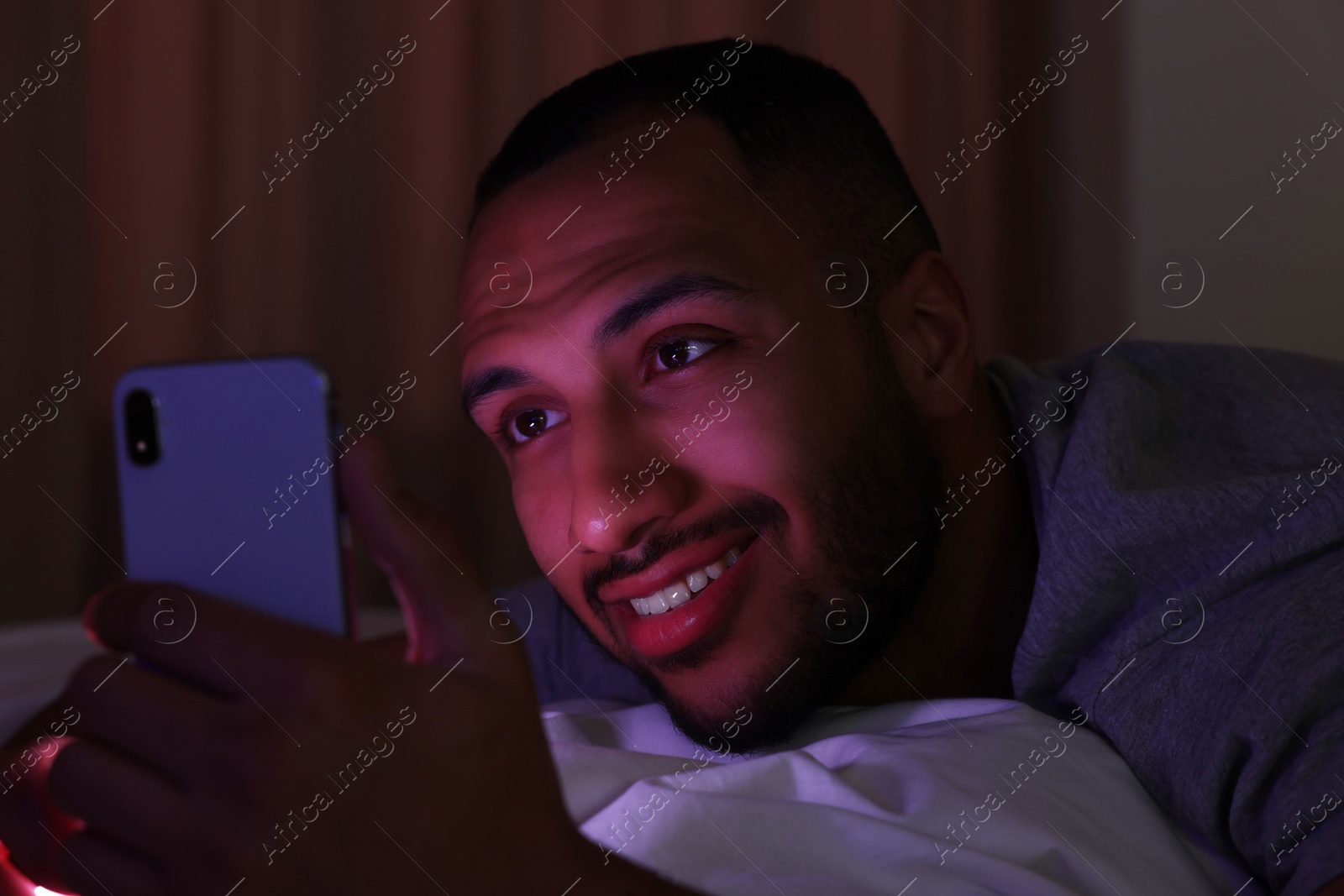 Photo of Young man using smartphone in bed at night. Internet addiction