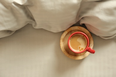 Photo of Cup of aromatic coffee on bed with soft blanket, top view