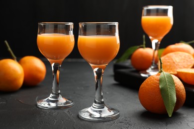 Photo of Tasty tangerine liqueur in glasses and fresh citrus fruits on black textured table