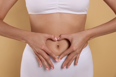 Photo of Woman in underwear making heart with hands on her belly against beige background, closeup. Healthy stomach