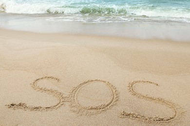 Message SOS drawn on sand near sea, above view