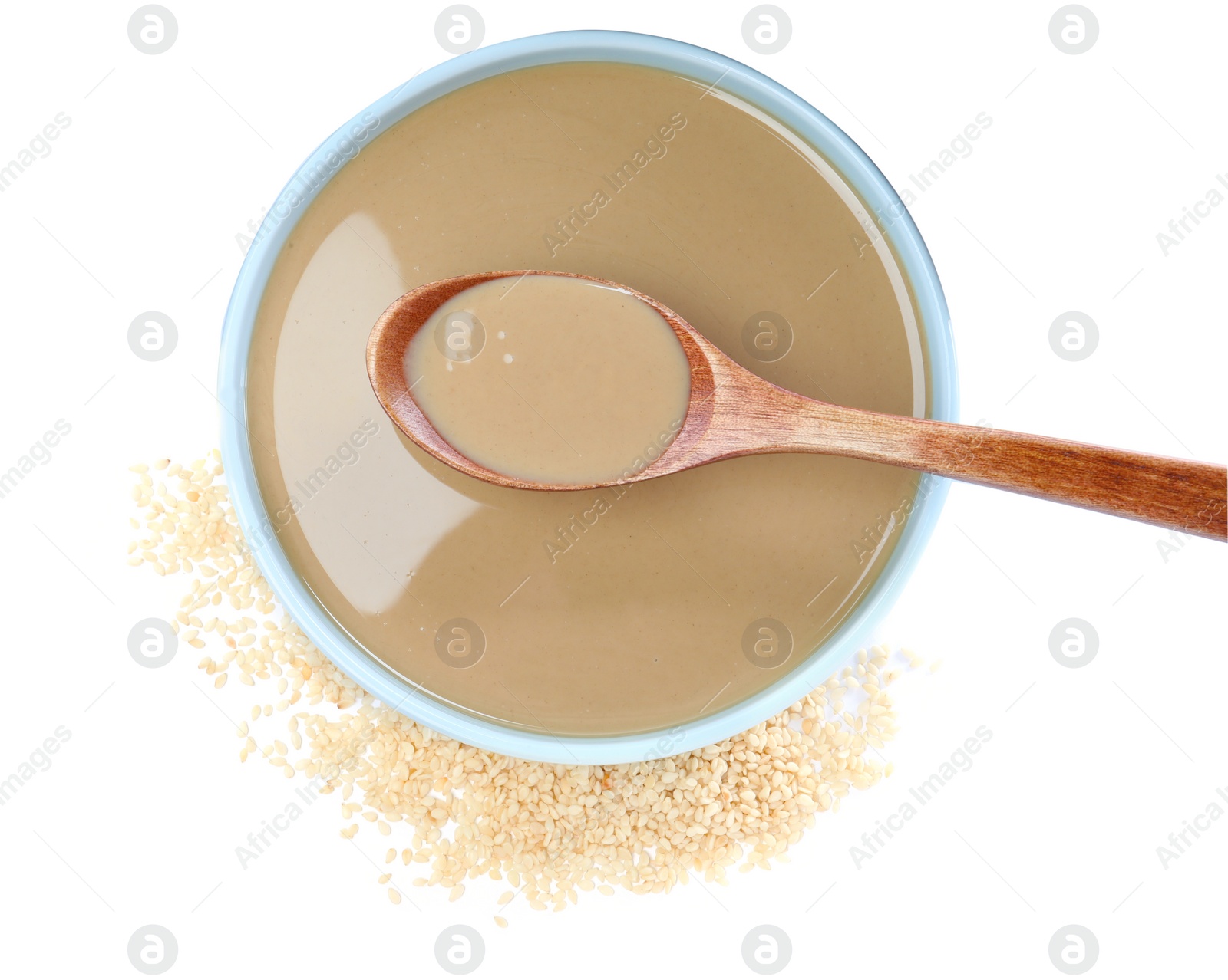 Photo of Spoon of tasty sesame paste above bowl and seeds on white background, top view