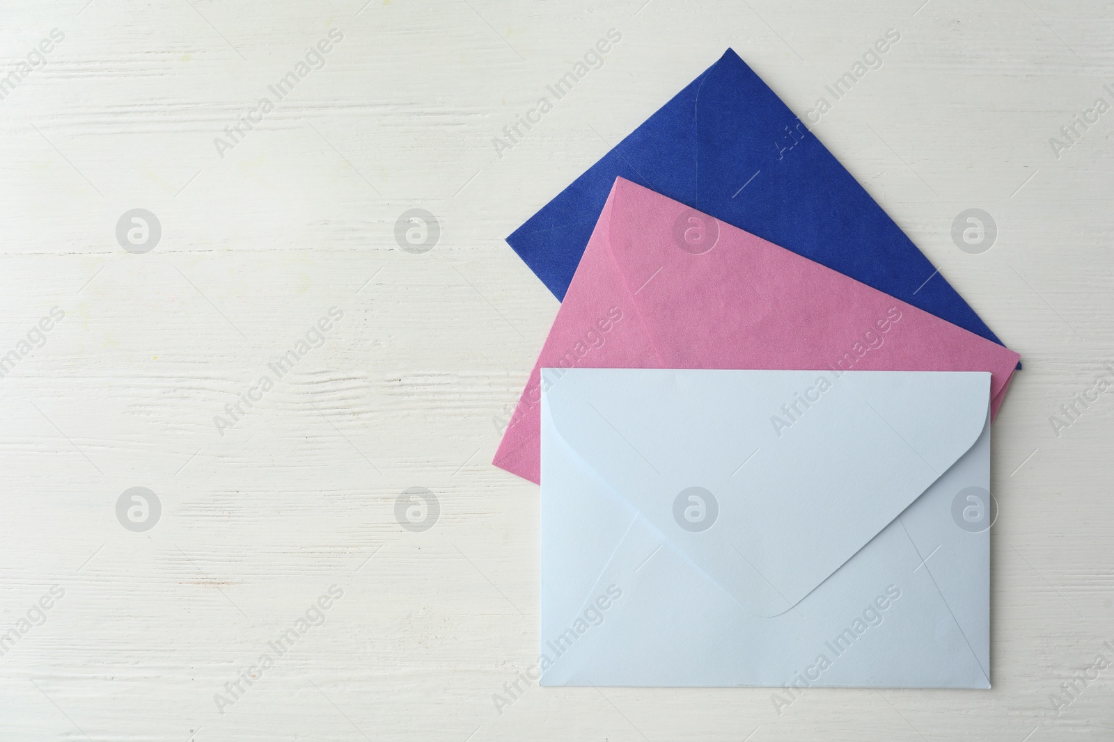 Photo of Colorful paper envelopes on white wooden table, flat lay. Space for text