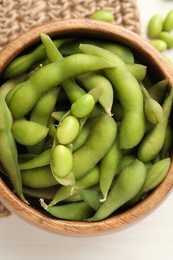 Photo of Bowl with green edamame beans in pods on white wooden table, top view