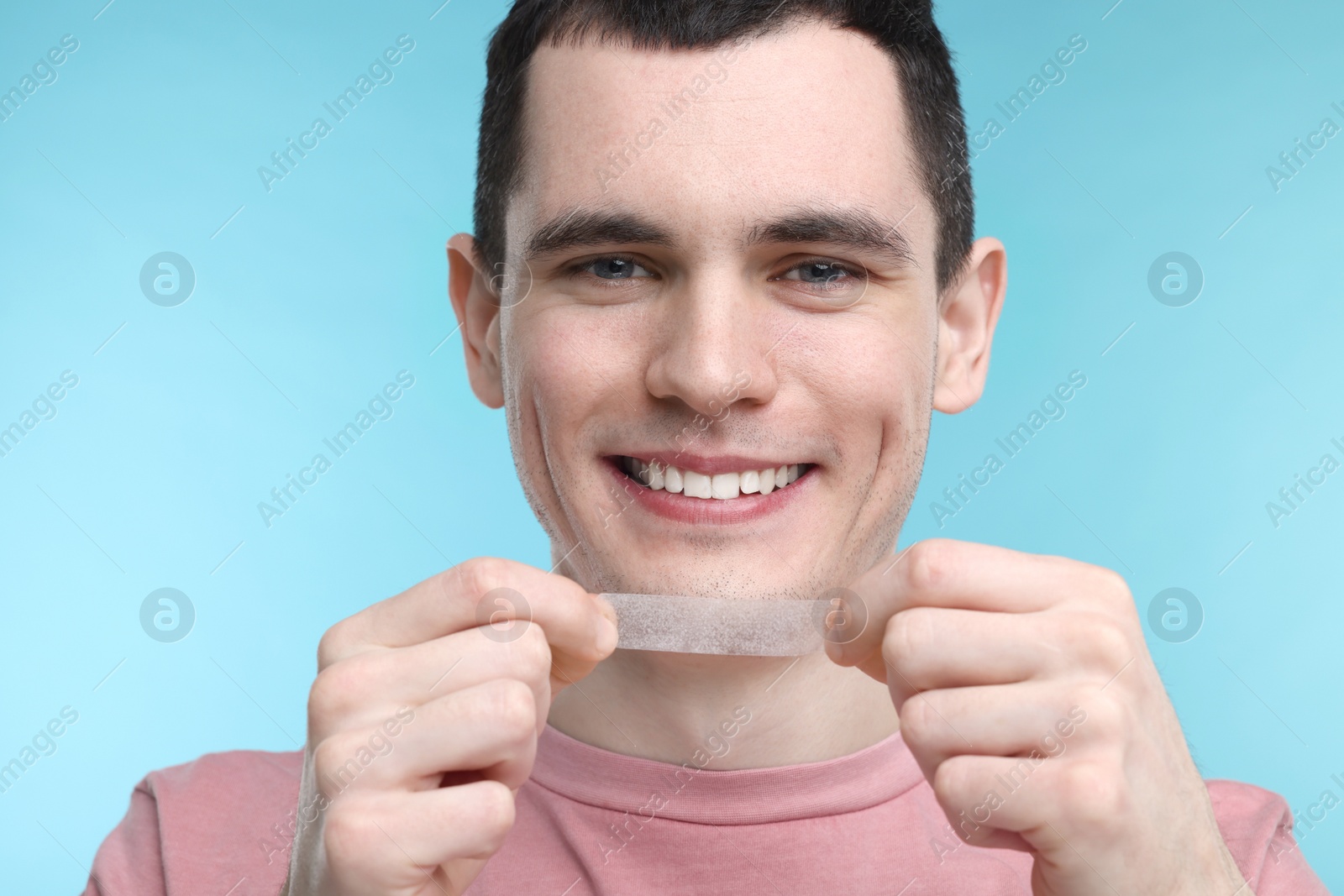 Photo of Young man with whitening strip on light blue background