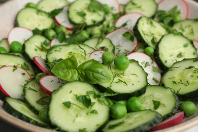 Photo of Appetizing salad with cucumbers, radish and pea in bowl, closeup
