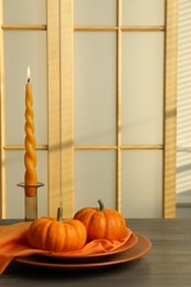 Burning candle and fresh pumpkins on wooden table indoors