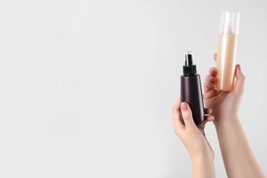 Photo of Woman holding spray bottles with hair thermal protection on white background, closeup. Space for text