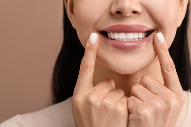 Photo of Woman showing her clean teeth and smiling on beige background, closeup