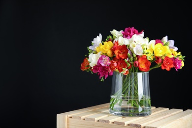 Photo of Bouquet of spring freesia flowers in vase on dark background. Space for text