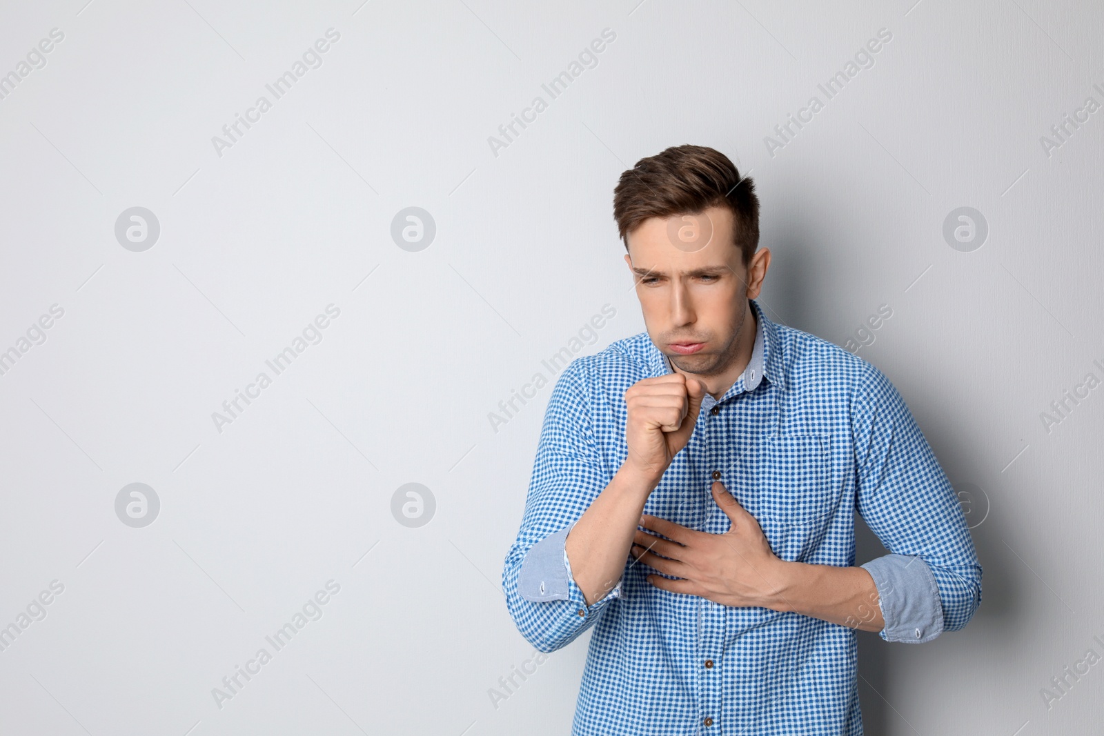 Photo of Young man coughing on light background