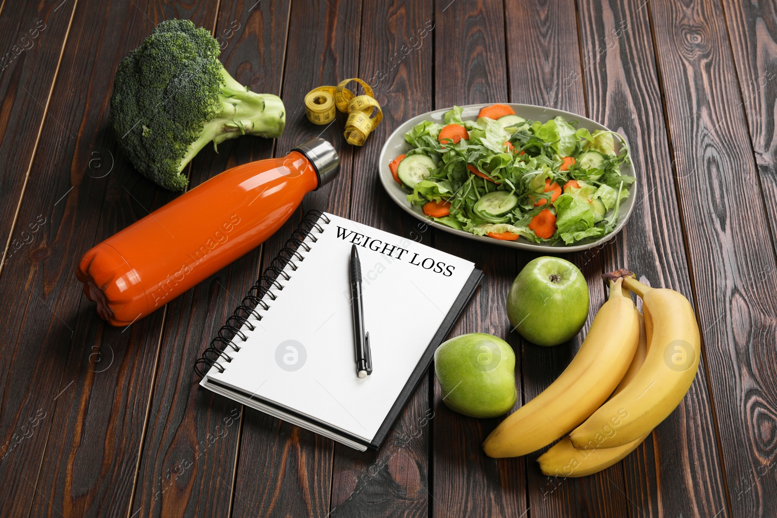 Photo of Notebook with phrase Weight Loss, bottle and different products on wooden table