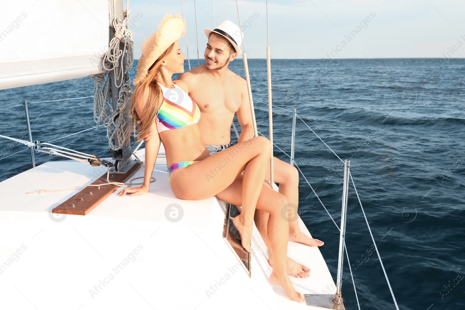 Photo of Young man and his beautiful girlfriend in bikini sitting on yacht. Happy couple on vacation