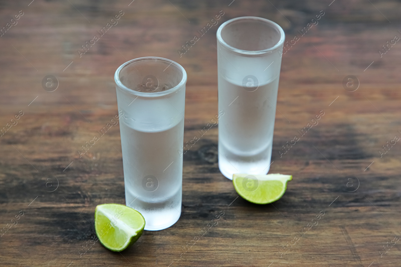 Photo of Mexican tequila shots with lime slices on wooden table. Drink made from agave