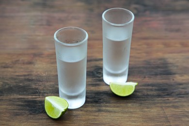 Photo of Mexican tequila shots with lime slices on wooden table. Drink made from agave