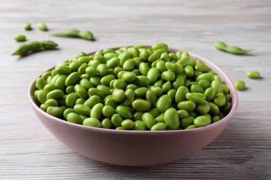 Photo of Bowl of delicious edamame beans on light wooden table