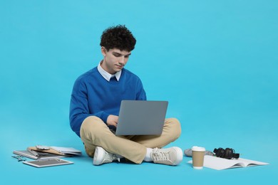 Portrait of student with laptop and stationery on light blue background
