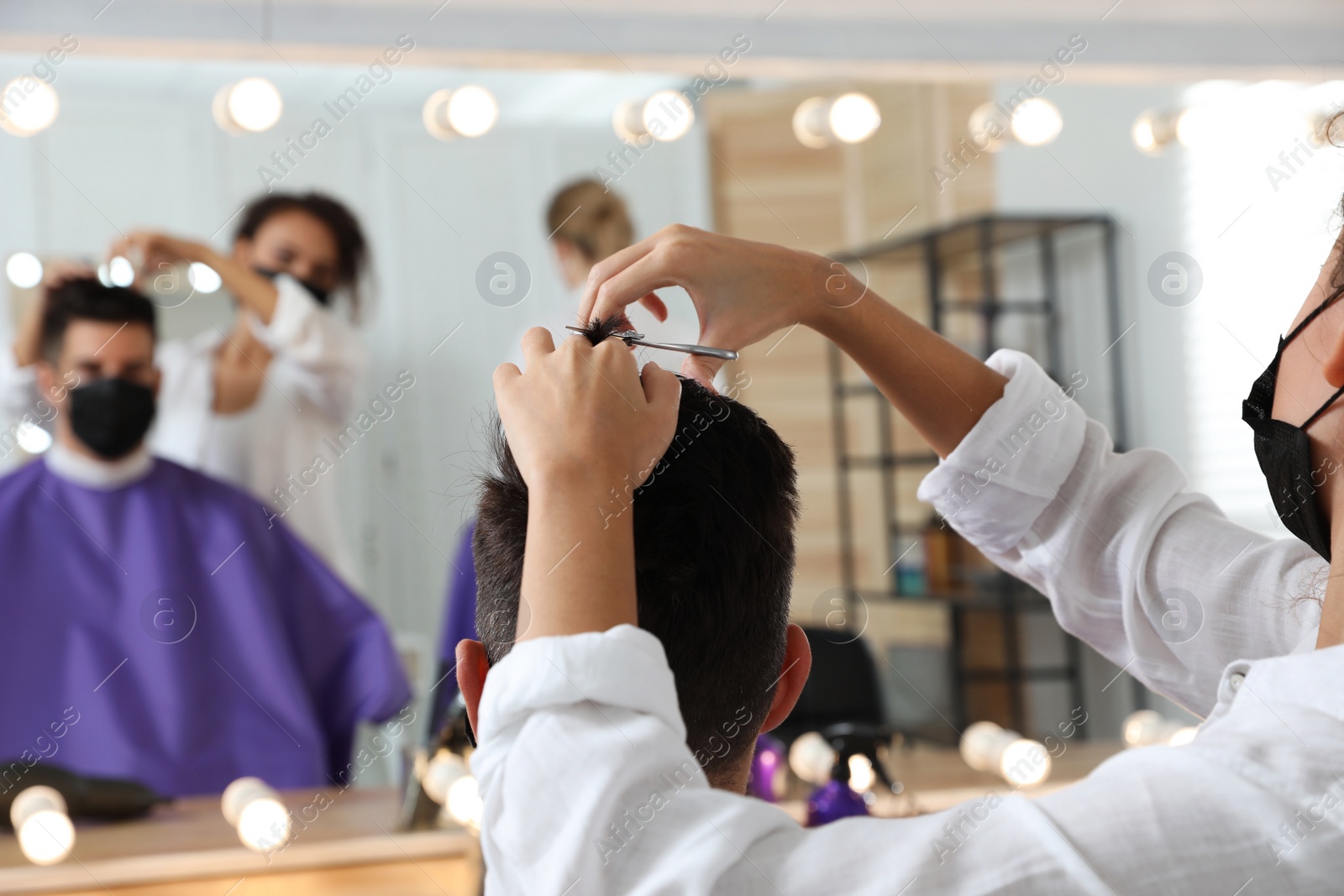 Photo of Professional stylist working with client in salon, closeup. Hairdressing services during Coronavirus quarantine