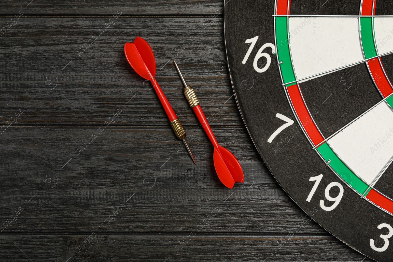 Photo of Dart board with color arrows on black wooden background, top view. Space for text