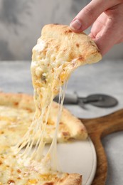 Woman taking piece of delicious cheese pizza at light grey table, closeup