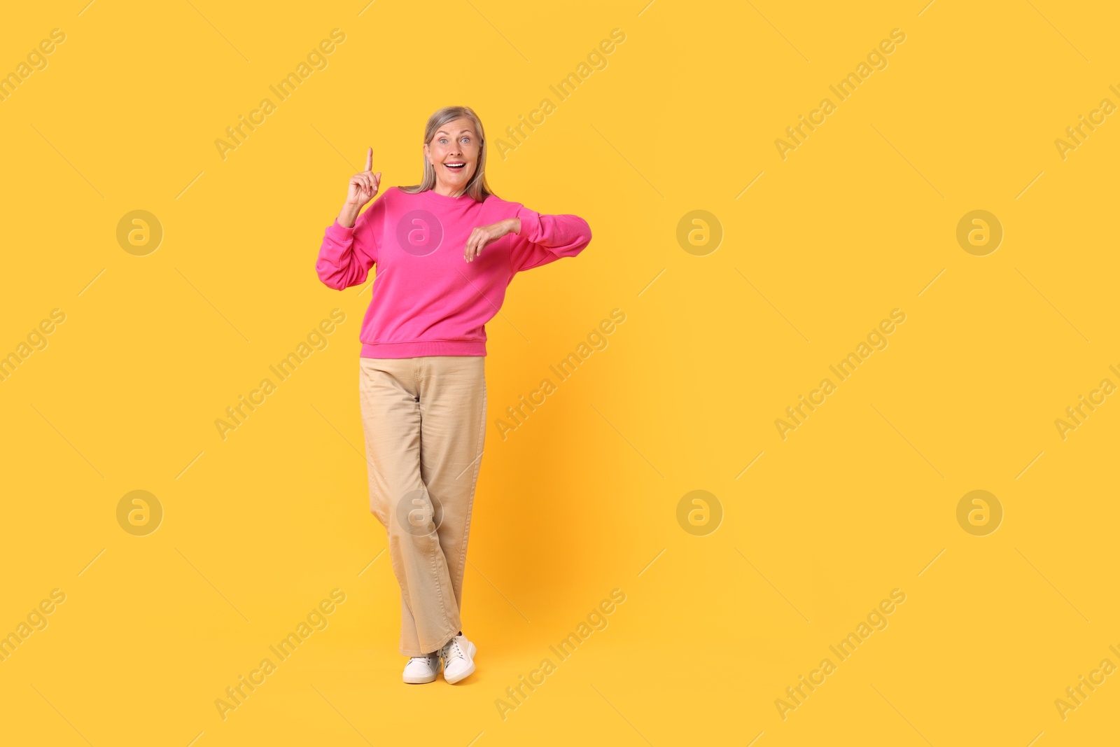 Photo of Happy senior woman pointing on orange background, space for text