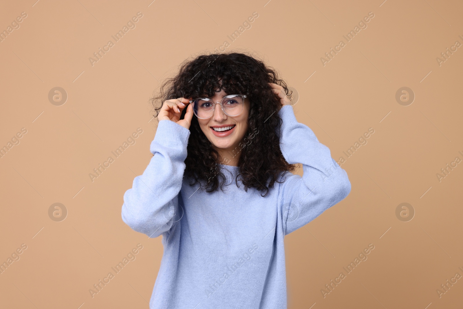 Photo of Happy young woman in stylish light blue sweater and glasses on beige background