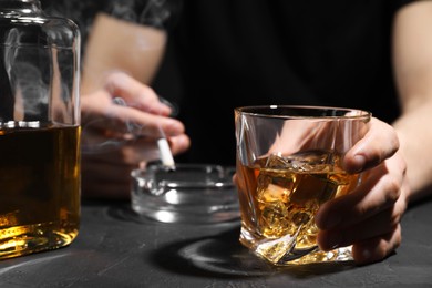 Photo of Alcohol addiction. Man with glass of whiskey and smoldering cigarette at dark textured table, selective focus