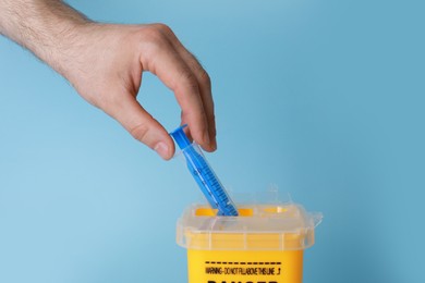 Photo of Man throwing used syringe into sharps container on light blue background, closeup