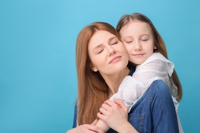 Portrait of happy mother and her cute daughter on light blue background. Space for text