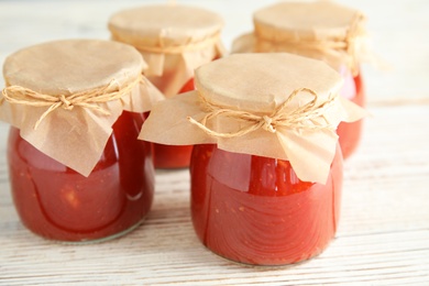 Photo of Jars of tomato sauce on wooden table, closeup