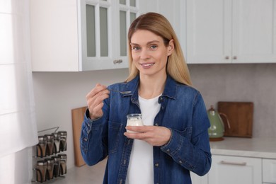 Woman eating tasty yogurt with spoon in kitchen