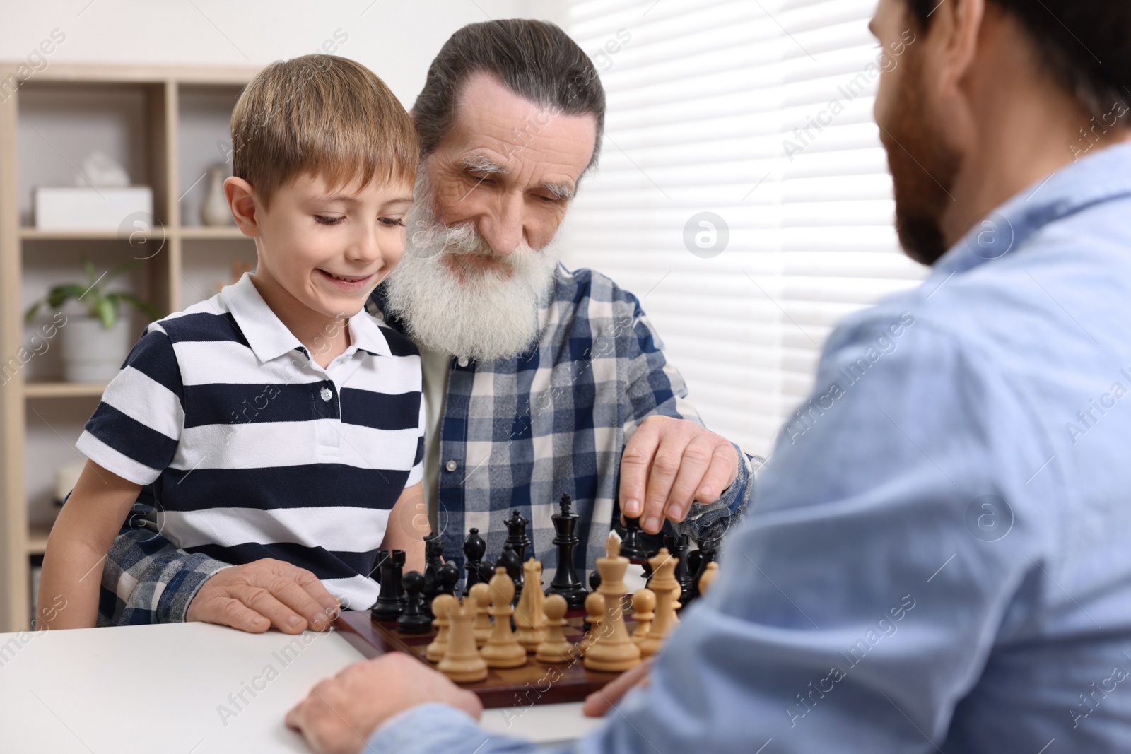 Photo of Family playing chess together at table in room