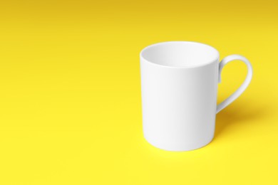 Photo of One white ceramic mug on yellow background, space for text