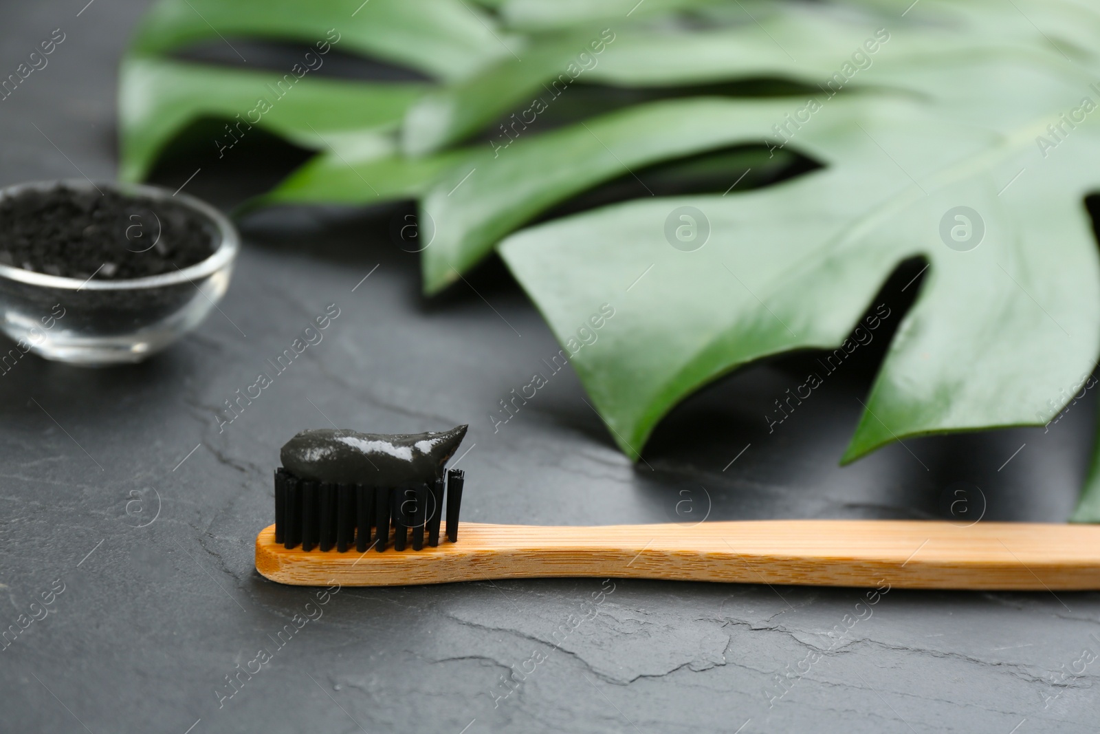 Photo of Bamboo toothbrush with charcoal paste on black stone table, closeup. Space for text