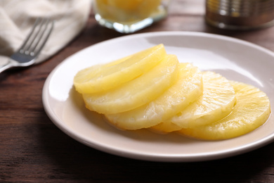 Photo of Tasty canned pineapple slices on wooden table, closeup