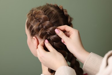 Photo of Professional stylist braiding woman's hair on olive background, closeup