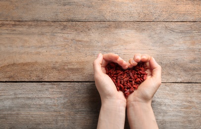 Photo of Woman holding goji berries on wooden background, top view with space for text. Heart health