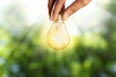 Image of Solar energy concept. Man holding glowing light bulb against green blurred background, closeup