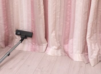 Photo of Removing dust from beautiful curtains with professional vacuum cleaner indoors