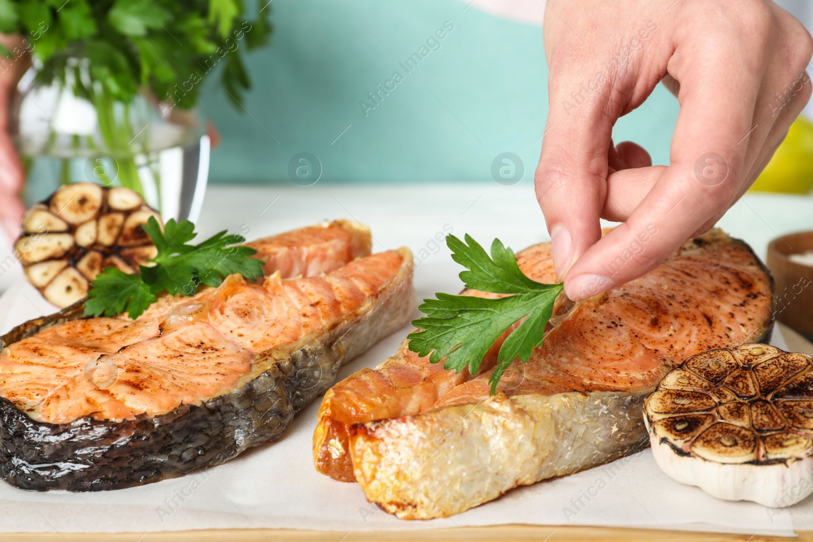 Photo of Woman adding parsley to cooked red fish on table, closeup