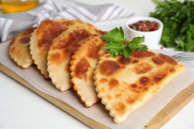 Photo of Board with delicious fried chebureki and parsley on white table