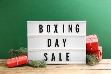 Composition with Boxing Day Sale sign and Christmas gifts on wooden table against green background
