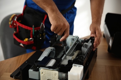 Photo of Repairman with screwdriver fixing modern printer indoors, closeup