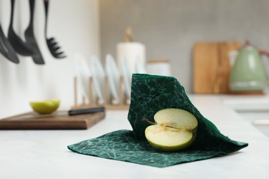 Photo of Half of apple with green beeswax food wrap on white table