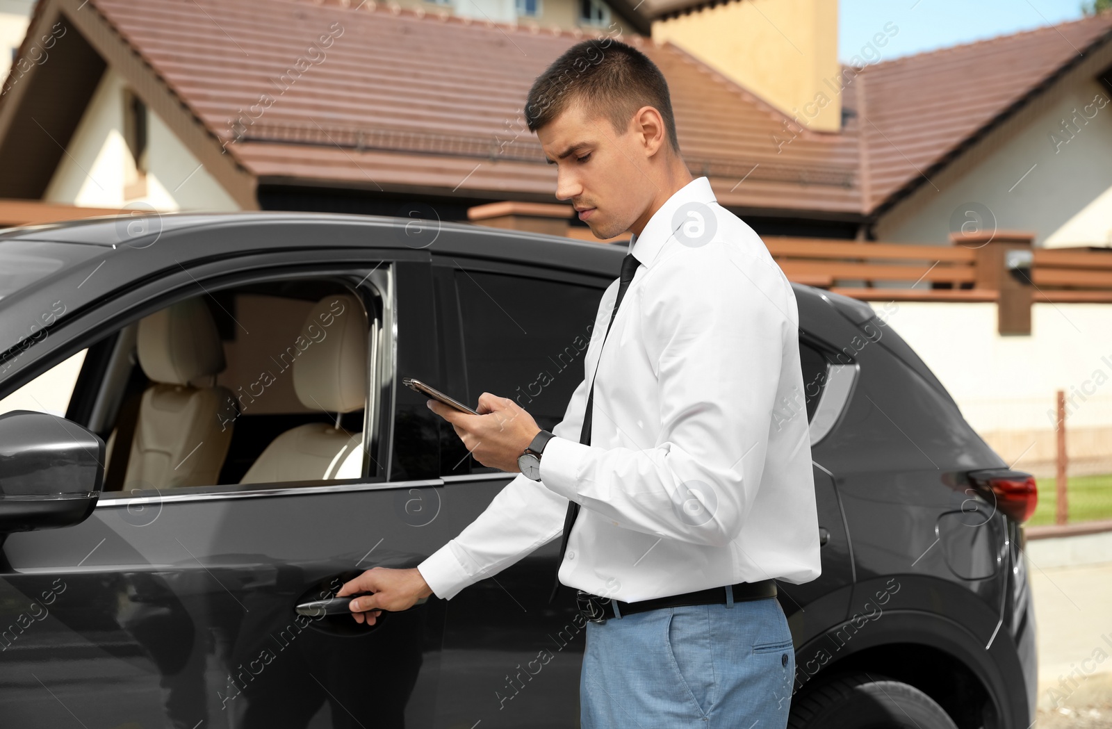 Photo of Attractive young man with smartphone near luxury car outdoors