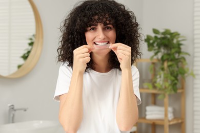 Photo of Young woman applying whitening strip on her teeth in bathroom